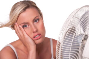 Overheated woman looking frustrated while using a fan, possibly due to central heating issues.